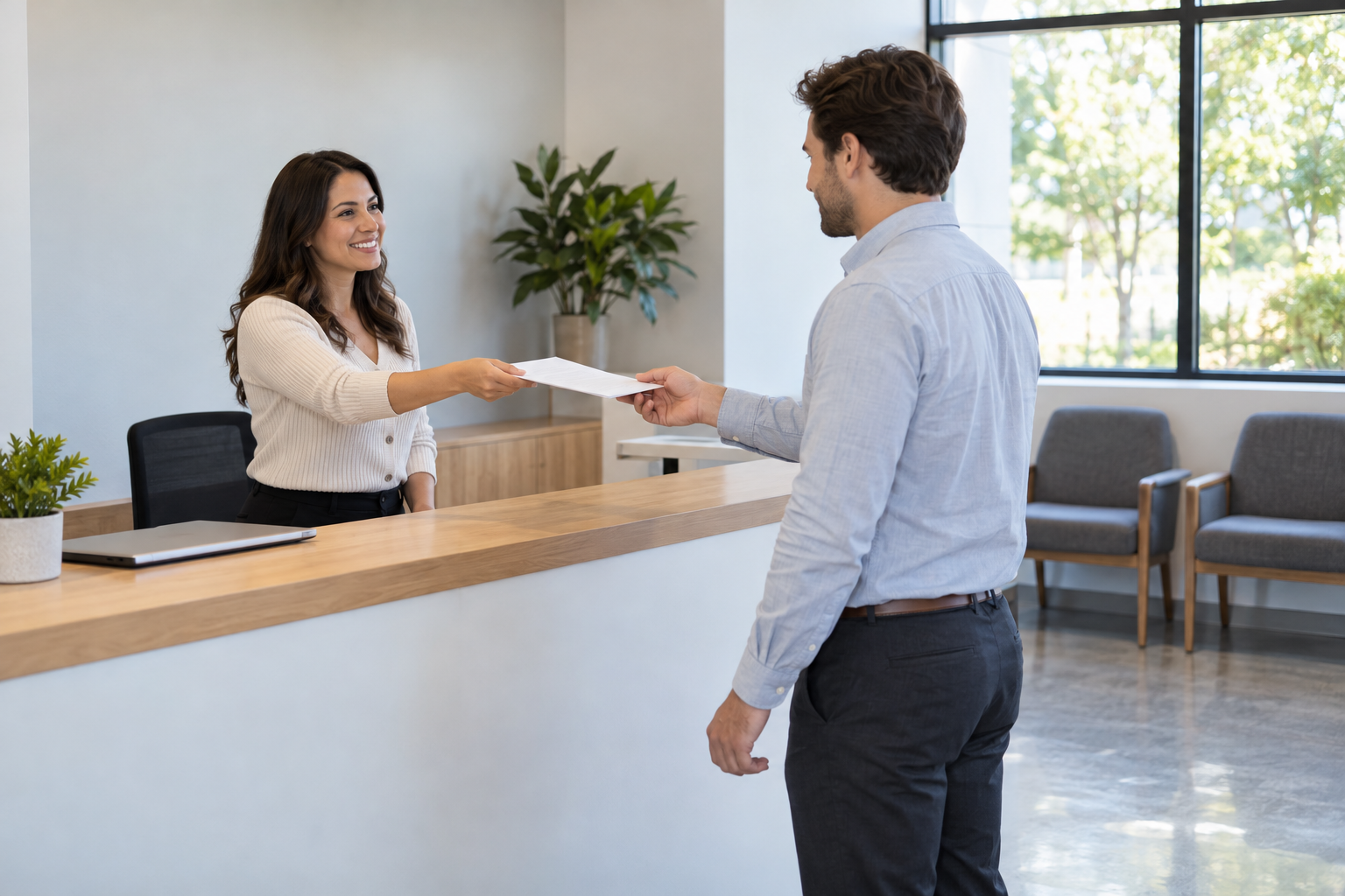 Ảnh luyện tập: một phụ nữ đứng sau quầy đưa tài liệu cho người đàn ông; có cây, laptop đóng và hai ghế trống cạnh cửa sổ.